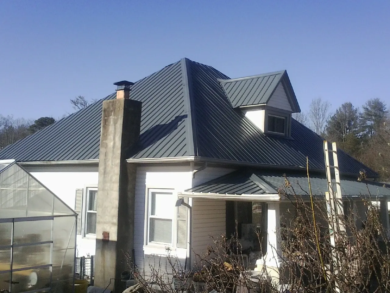 Dark blue standing seam metal roof on a white farmhouse with dormer — Slate & Tile Roof Repair by Roofing Brothers in Greenwich