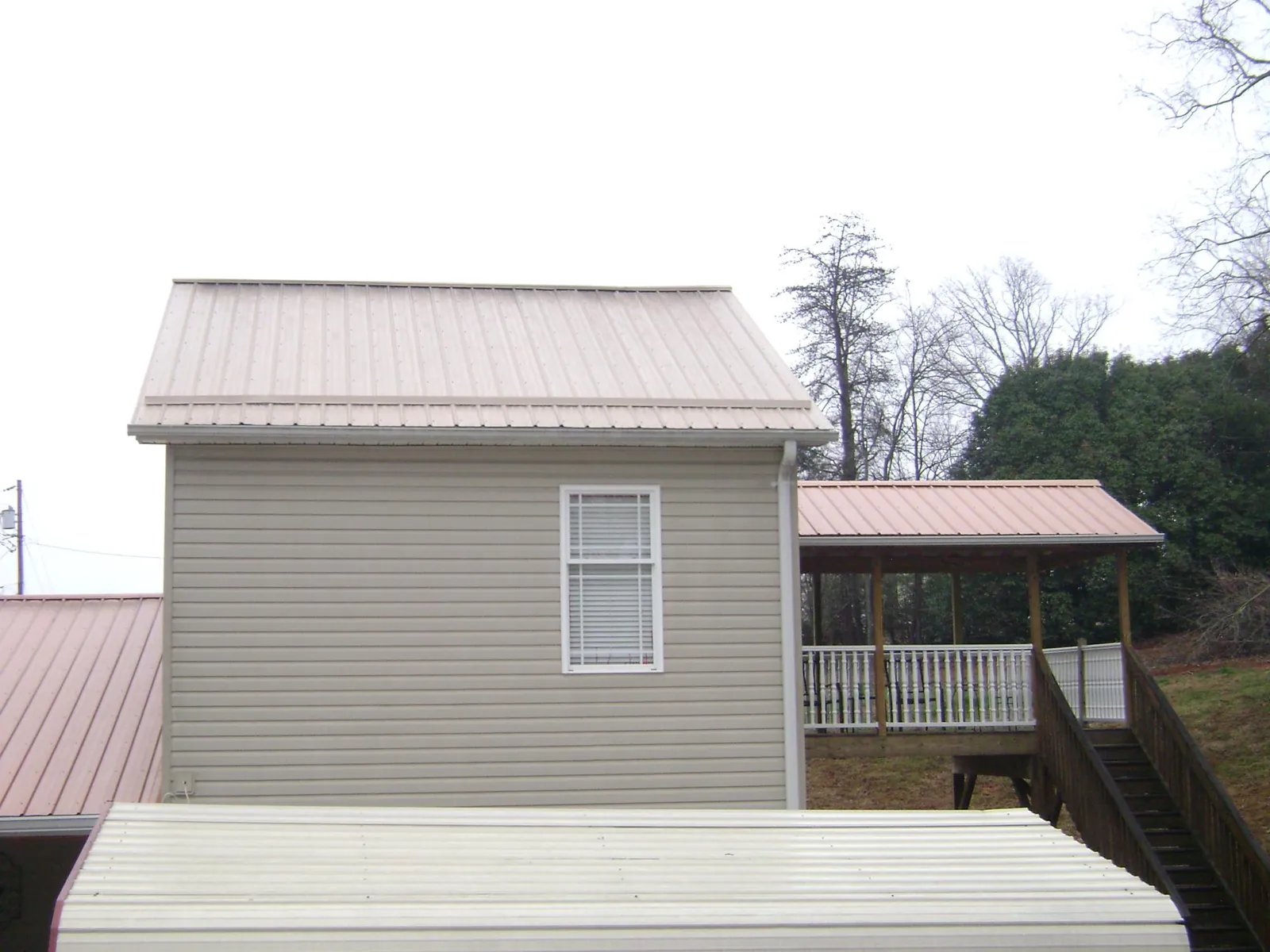 Tan metal roofs on a two story addition and attached porch, from a Roof Replacement job in Greenwich